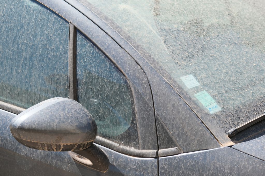 Retrovizor, bočni prozori i vjetrobran tamnog automobila prošarani osušenim mrljama saharske prašine